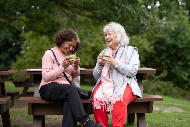 Two elderly ladies sitting on a bench having a coffee